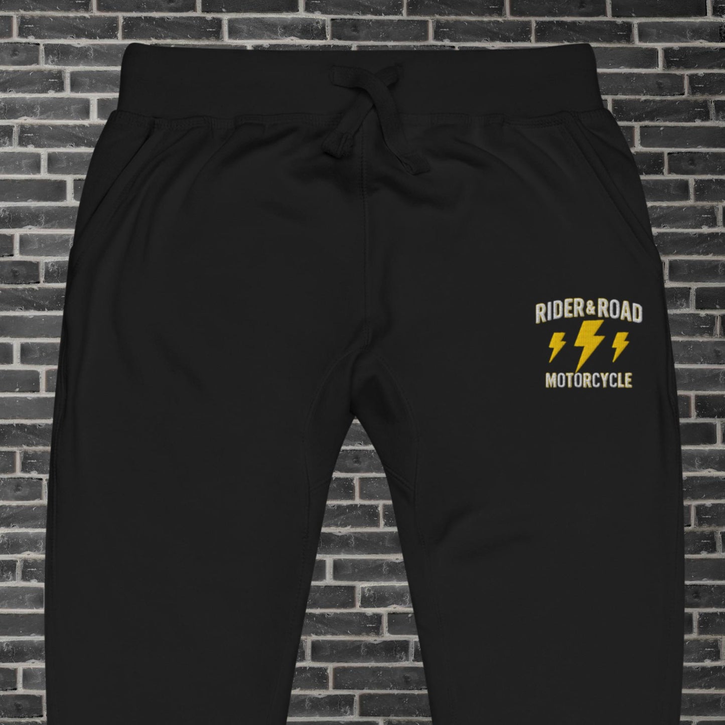 "Pantalon de chandal de felpa en color negro con bordado en pierna izquierda de la frase Rider & Road Motorcycle con rayos amarillos debajo - Black fleece tracksuit trousers with the phrase “Rider & Road Motorcycle” embroidered on the left leg with yellow lightning bolts underneath"