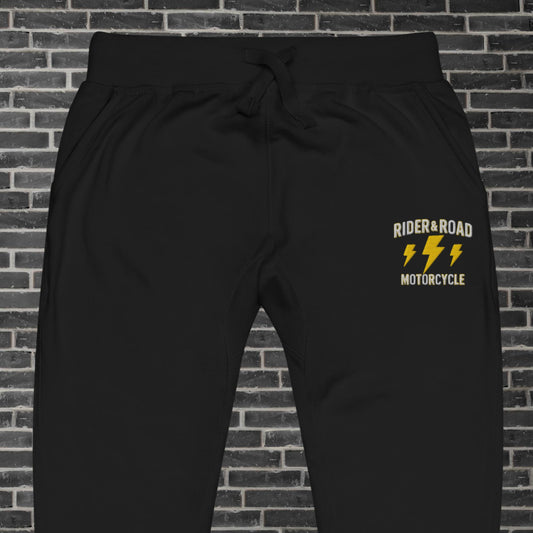 "Pantalon de chandal de felpa en color negro con bordado en pierna izquierda de la frase Rider & Road Motorcycle con rayos amarillos debajo - Black fleece tracksuit trousers with the phrase “Rider & Road Motorcycle” embroidered on the left leg with yellow lightning bolts underneath"